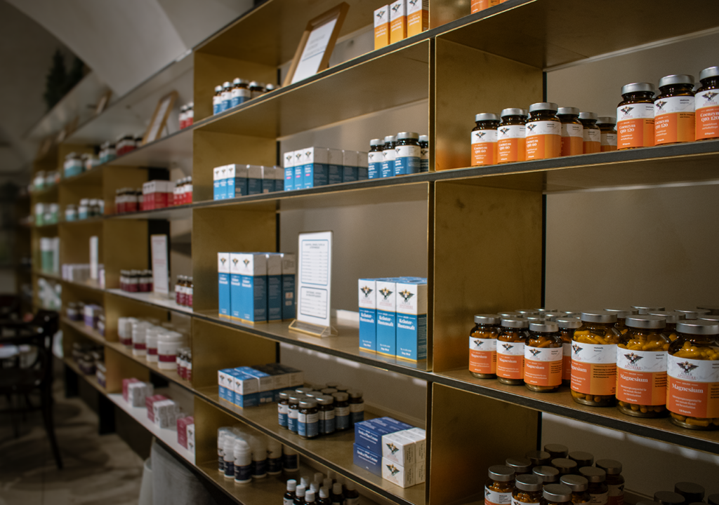 Blick auf ein Regal in der Adler Apotheke mit verschiedenen Grazer Hausspetzialitäten. Die Regale sind ordentlich angeordnet und zeigen unterschiedliche Flaschen und Verpackungen in diversen Farben, insbesondere in Orange, Blau und Lila.
