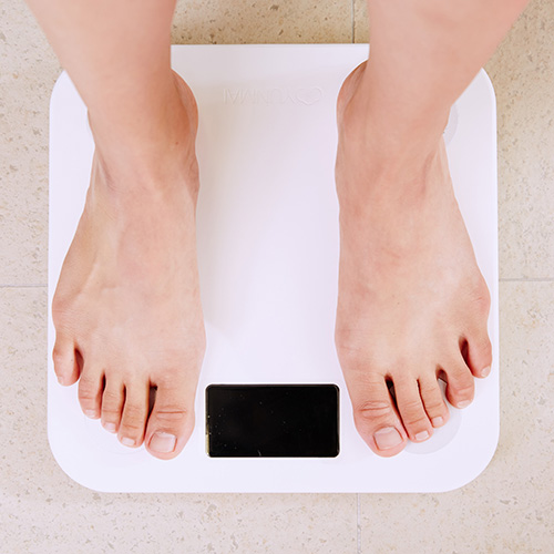 Zwei Füße stehen auf einer digitalen Personenwaage, die auf einem hellen Boden platziert ist.