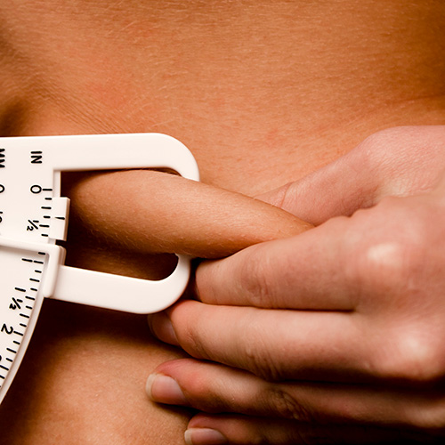 Eine Person verwendet eine Hautfaltendickemesszange, um die Hautfalte am Oberkörper zu messen, während eine Hand die Zange hält und die andere einen Hautbereich zusammendrückt.