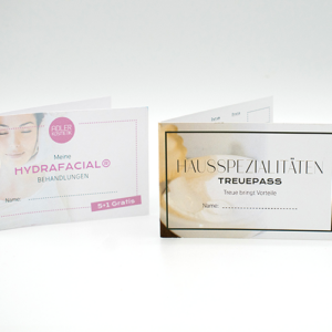 Zwei Faltkarten, eine für "HYDRAFACIAL® BEHANDLUNGEN" mit dem Hinweis "5+1 Gratis" und die andere für "HAUSSPEZIALITÄTEN" mit dem Titel "TREUEPASS". Beide Karten enthalten Platz für einen Namen und vermitteln Informationen über Angebote der Adler Apotheke.