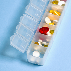 Transparentes Tabletten-Organizer mit verschiedenen Vitaminen und Medikamenten in Fächern.