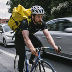 Ein Radbote hat einen gelben Rucksack am Rücken und fährt gerade durch die Grazer Innenstadt.
