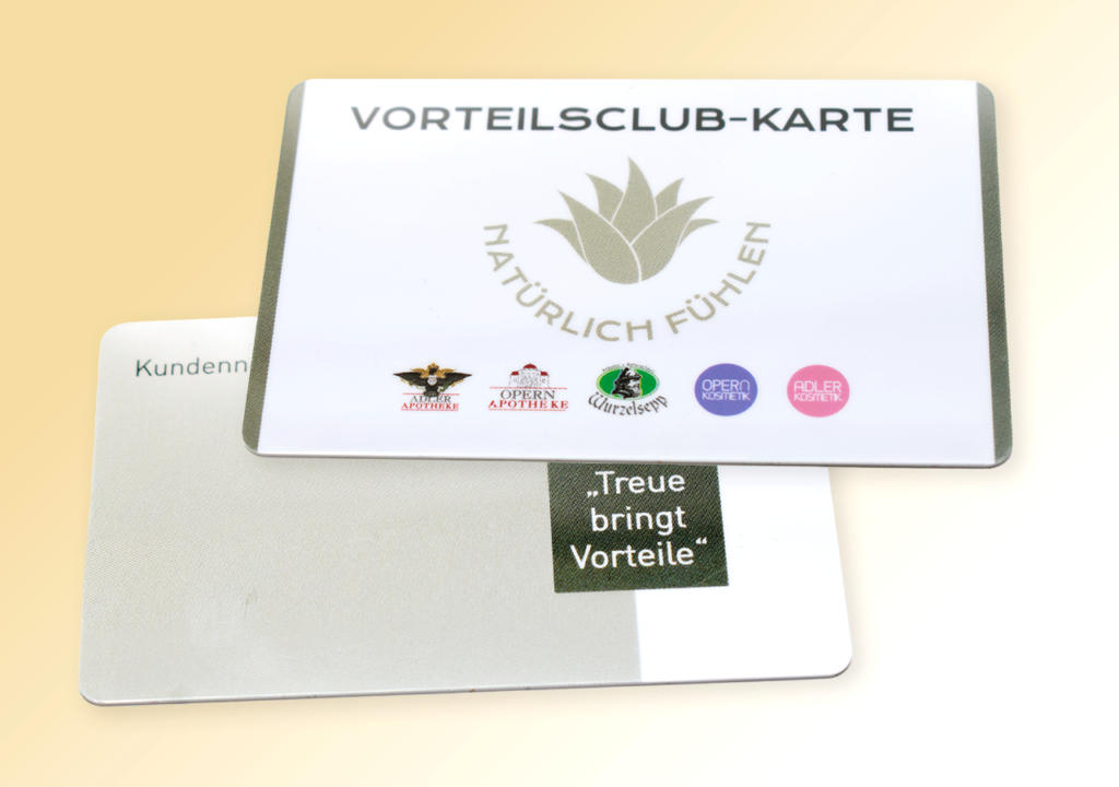 wei übereinanderliegende Vorteilskarten vor hellem Hintergrund; oben die weiße „VORTEILSCLUB‑KARTE“ mit Blattlogo, dem Schriftzug „NATÜRLICH FÜHLEN“ und einer Reihe kleiner Logos (Adler Apotheken, Opern‑Apotheken, Wurzelsepp, Adler Kosmetik, Opern Kosmetik), unten die Rückseite mit dem Textfeld „Treue bringt Vorteile“.