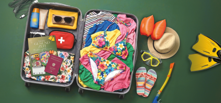 Meine GESUNDZEIT Frühling und Sommer. Ausgabe 1 2026. Ein offener Koffer mit verschieden Inhalten für Reisen: ein Bikini, rosa T-shirts, blauer T-Shirt, eine Sonnenbrille, Sonnencreme, Reisepass, Fotoapparat, , buntes T-Shirt, erste Hilfe Tasche, . Neben den offenen Koffer liegen eine Tauschbrille, eine Schnorchel, Schwimmflügel, Hut, offene Sandalen. Unten stehen die Themen: Reiseapotheke, Durstlöscher für die Haut, Allergien